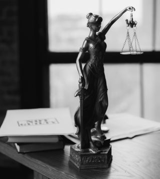 Grayscale photo of Lady Justice statue beside legal documents on a wooden table.